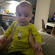 Mattia a rejoint le concours — aidez-le/la à gagner de superbes lots ! baby, child, person, indoor, kitchen, onesie, yellow_clothing, hands, clock, appliance, chair, table, television, furniture, light, face, smiling_bunny, holding, couch, curious