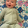 Joey is registered to the contest to win money with this photo: baby, child, smiling, onesie, quilt, toy, floor, carpet, playtime, happy, infant, cute, indoor, person, face, colorful, pattern, lying_down, cheerful, young_child