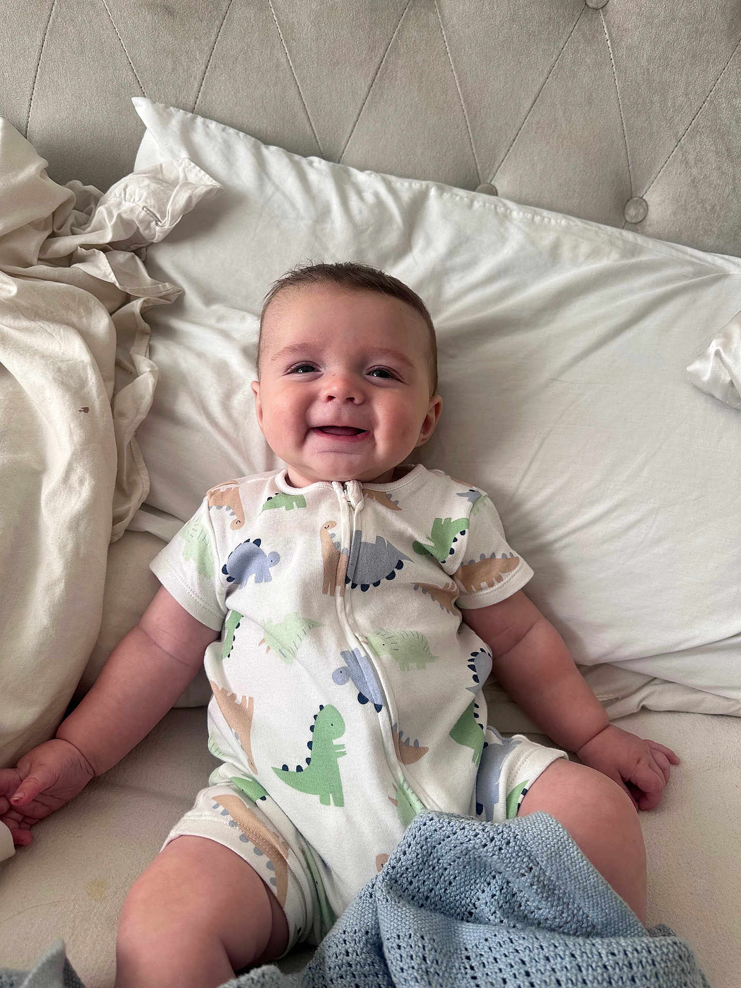 Joey joined the competition — help win amazing prizes! baby, smiling, dinosaur_onesie, bed, pillow, blanket, infant, child, happy, indoor, cute, portrait, sleepwear, cozy, soft_lighting, human, young_child, sitting, fabric, comfort