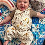 baby, smiling, tongue_out, patchwork_quilt, plush_toy, rainbow_pillow, animal_print, overalls, infant, child, happy, cute, face, lying_down, fabric, soft_toy, colorful, playtime, indoors, person