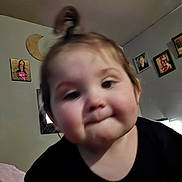 Madi joined the competition — help win amazing prizes! toddler, child, face, portrait, black_shirt, hair_tie, indoor, wall, picture_frame, decor, family_photo, crescent_moon, expression, close_up, blur, young_child, person, smile, baby, room