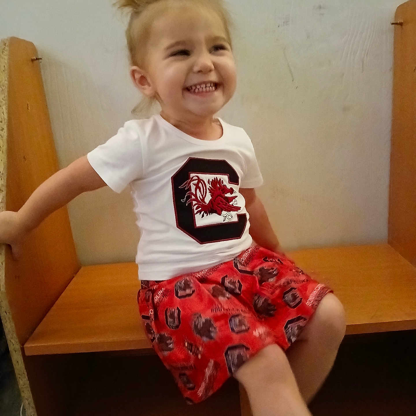 Kennedy is registered to the contest to win money with this photo: bodypart, child, clothing, couch, face, female, furniture, girl, happy, head, laughing, mouth, person, photography, portrait, shorts, sitting, skirt, t_shirt, wood
