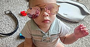 Jamir is registered to the contest to win money with this photo: aviator_sunglasses, baby, carpet, casual_clothing, child, face, fashion, indoor, photographer, play_mat, playroom, portrait, reflection, serious_expression, shorts, sitting, storage_bins, sunglasses, toddler, toy