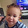 Jamir is registered to the contest to win money with this photo: baby, carpet, child, close_up, curly_hair, cute, face, furniture, happy, home, indoor, living_room, photograph, portrait, remote_control, smiling, striped_shirt, television, toddler, toy