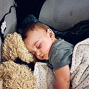 Rider is registered to the contest to win money with this photo: baby, blanket, child, close_up, comfort, cozy, cute, gray_shirt, indoor, infant, peaceful, playpen, plush_toy, polka_dots, portrait, relaxation, resting, sleeping, soft_lighting, teddy_bear