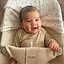 baby, smile, infant, face, clothing, onesie, babybjorn, seat, child, hand, blanket, wooden_floor, happy, cute, young_child, indoors, portrait, sitting, baby_seat, comfort