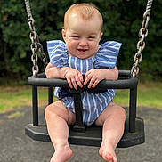 Olivia is registered to the contest to win money with this photo: baby, child, swing, outdoor, playground, smiling, happy, blue_clothing, striped_clothing, barefoot, grass, trees, metal_chains, seat, infant, cute, summer, fun, person, portrait