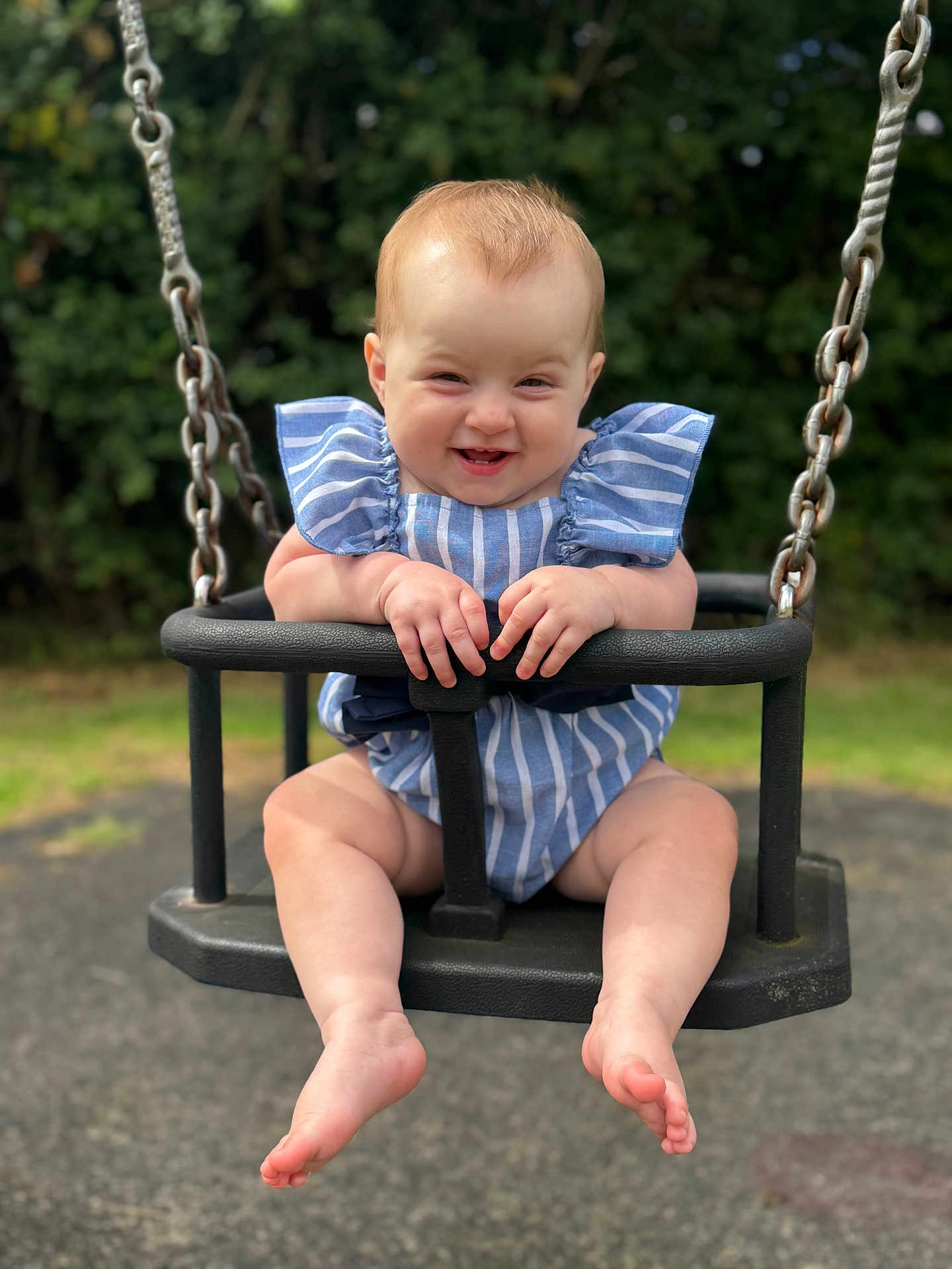 Olivia is registered to the contest to win money with this photo: baby, child, swing, outdoor, playground, smiling, happy, blue_clothing, striped_clothing, barefoot, grass, trees, metal_chains, seat, infant, cute, summer, fun, person, portrait