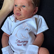 Maya joined the competition — help win amazing prizes! newborn, baby, infant, onesie, mittens, white_clothing, bunny, embroidered_text, hand, resting, cute, baby_garment, portrait, indoor, soft_lighting, skin, face, person, newborn_clothes, tender_moment