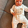 baby, infant, onesie, hat, bear_ears, couch, gray_couch, heart_pattern, plush_bear_face, child, cute, portrait, indoors, cozy, soft_lighting, chubby_cheeks, wide_eyes, laying_down, white_clothing, toddler