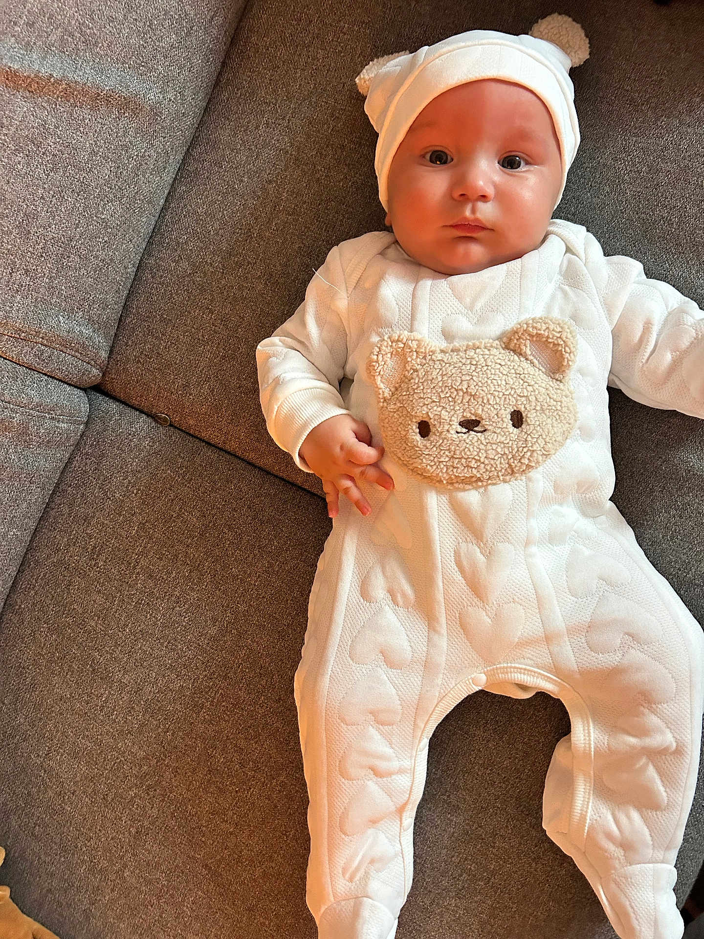 Aymen participe au concours pour gagner de l'argent avec cette photo : baby, infant, onesie, hat, bear_ears, couch, gray_couch, heart_pattern, plush_bear_face, child, cute, portrait, indoors, cozy, soft_lighting, chubby_cheeks, wide_eyes, laying_down, white_clothing, toddler