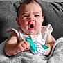 Maisie Jo is registered to the contest to win money with this photo: baby, infant, face, expression, mouth_open, hand, toy, teething_toy, blanket, couch, furniture, clothing, white_clothing, indoor, person, cute, child, skin, head, sitting