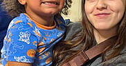 Ronald is registered to the contest to win money with this photo: child, smiling, curly_hair, blue_shirt, woman, nose_ring, hug, happy, indoor, portrait, person, casual_clothing, affection, family, closeup, candid, diverse, joy, toddler, young_adult