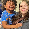 child, smiling, curly_hair, blue_shirt, woman, nose_ring, hug, happy, indoor, portrait, person, casual_clothing, affection, family, closeup, candid, diverse, joy, toddler, young_adult