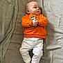 Rúben a rejoint le concours — aidez-le/la à gagner de superbes lots ! baby, infant, orange_sweatshirt, white_pants, white_socks, bed, blanket, fabric, lying_down, looking_away, cute, child, portrait, indoors, soft_texture, clothing, cozy, small_hands, expression, skin