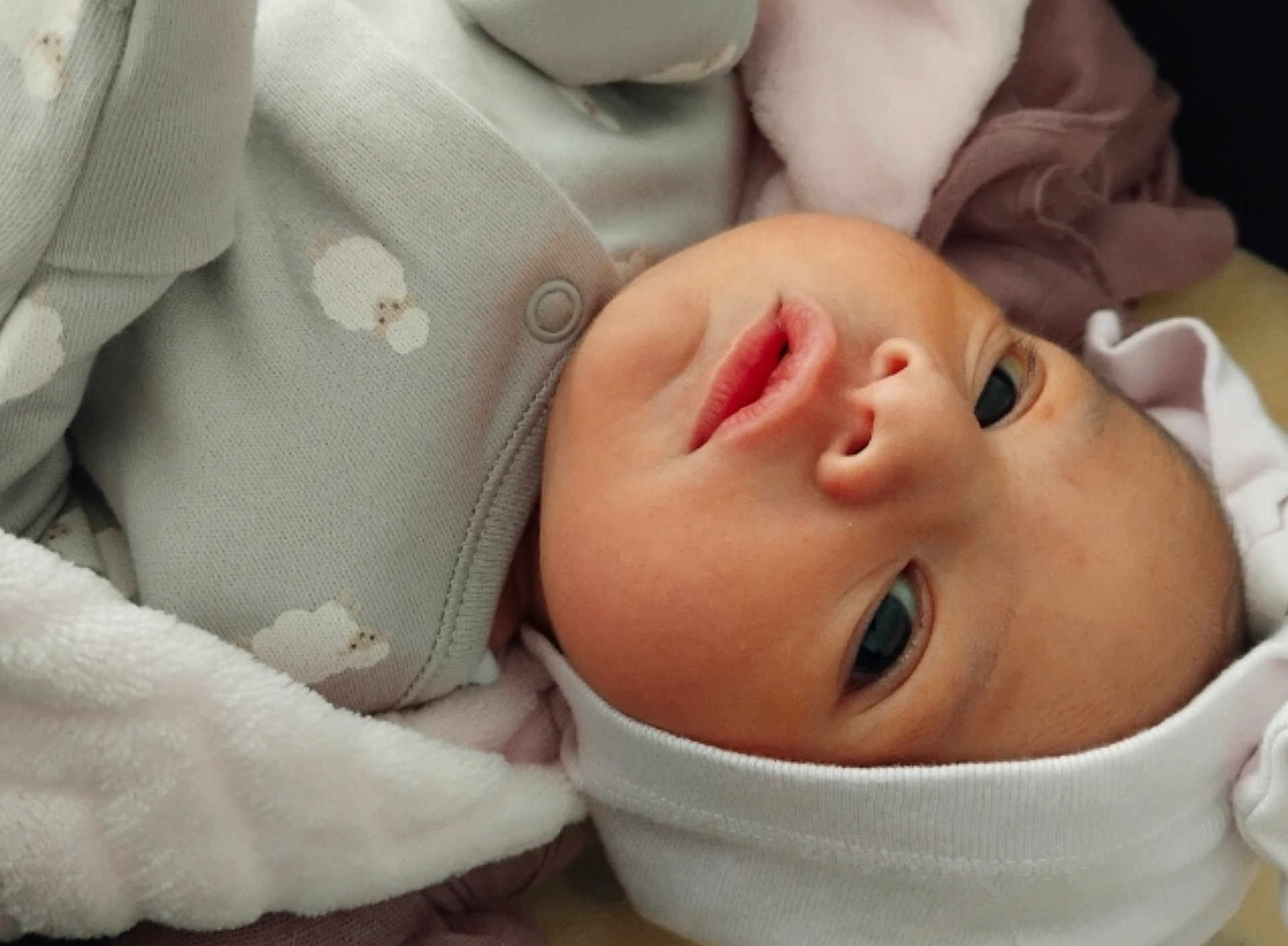 Ama is registered to the contest to win money with this photo: baby, infant, face, eyes, blanket, clothing, hat, newborn, skin, cute, soft, lying_down, cozy, portrait, expression, child, closeup, headwear, apparel, sleepwear