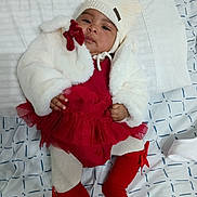 Emily joined the competition — help win amazing prizes! baby, infant, red_tutu, white_jacket, knit_hat, red_socks, bow, bedspread, patterned_bedding, cute, indoors, child, portrait, laying_down, warm_clothing, cozy, soft_toys, baby_fashion, newborn, adorable