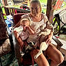 Liberty is registered to the contest to win money with this photo: woman, baby, dog, puppy, bottle, chair, porch, outdoor, smile, pet, leash, sneakers, wooden_furniture, carpet, relaxing, casual_clothing, greenery, daylight, house, family