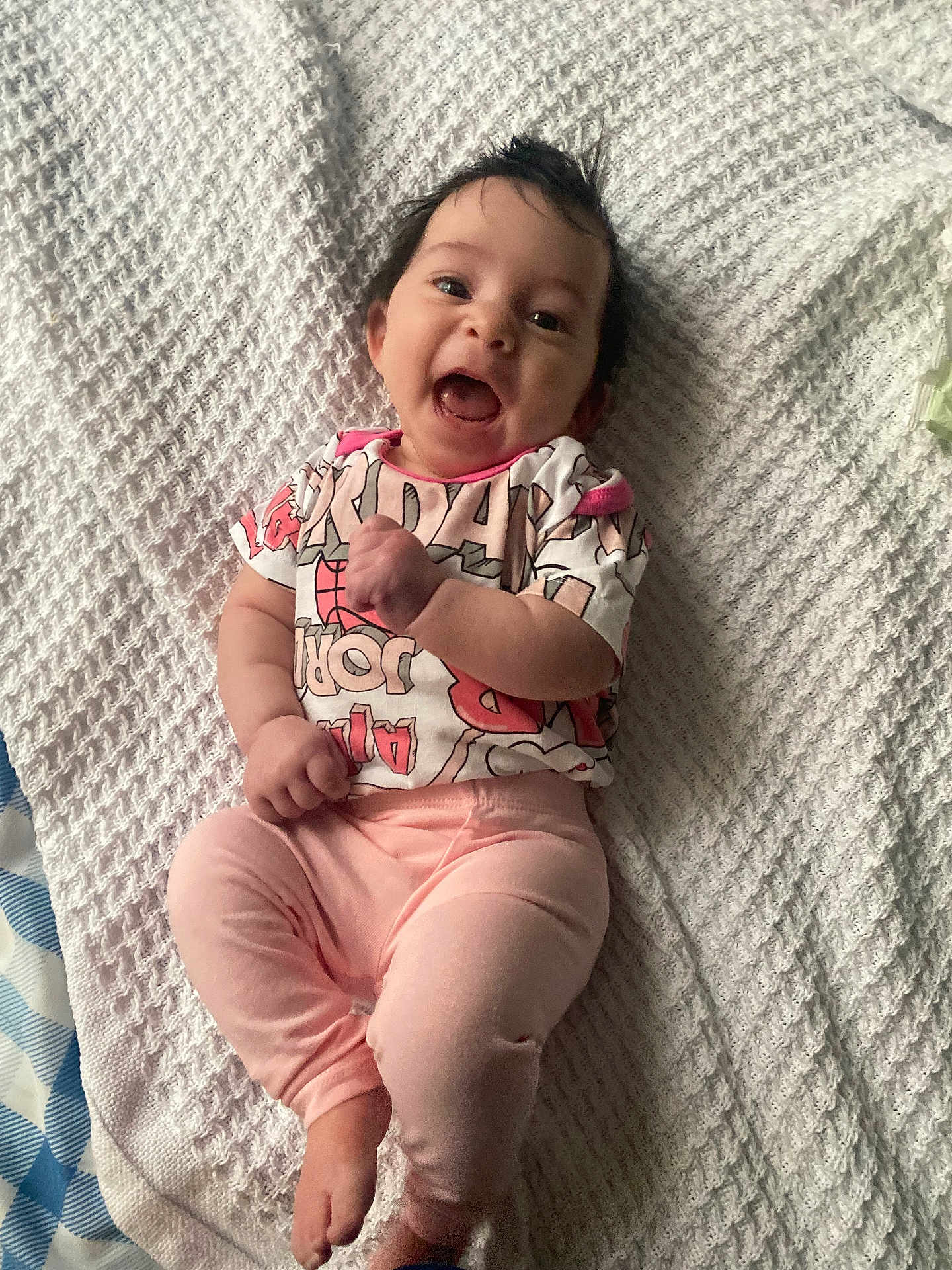 Rosalie is registered to the contest to win money with this photo: baby, infant, smile, laughing, face, eyes, hair, blanket, textured_blanket, onesie, pink_pants, laying_down, bed, cotton, cute, happy, mouth_open, hand, feet, portrait