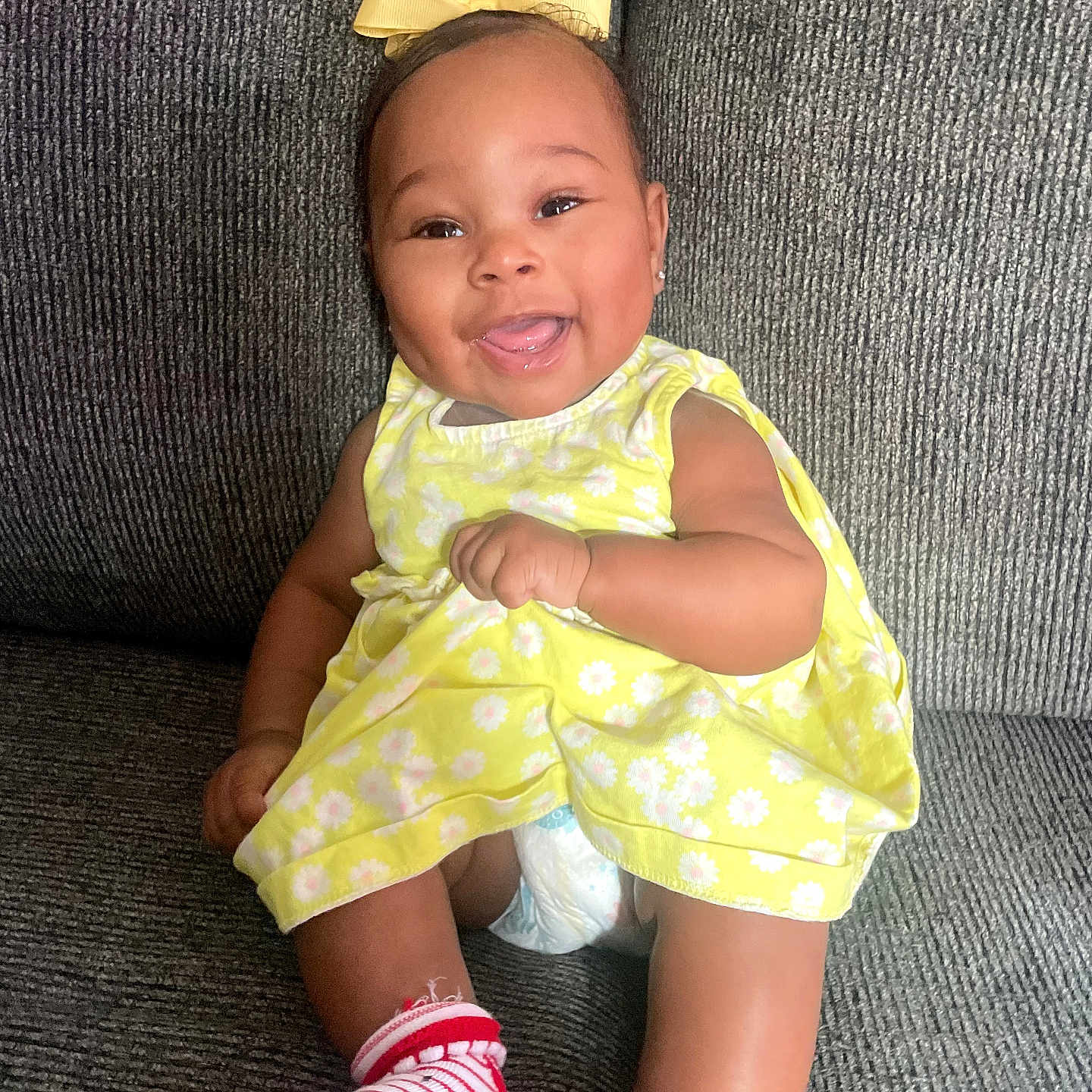 Leoni joined the competition — help win amazing prizes! baby, child, smiling, yellow_dress, bow, socks, red, white, couch, gray, happy, infant, cute, portrait, seated, indoor, person, clothing, diaper, baby_girl