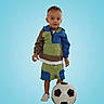 Kobi is registered to the contest to win money with this photo: child, boy, soccer, football, ball, sports, sporty, portrait, studio, blue_background, standing, outdoor_style, colorful_clothing, hooded_jacket, shorts, sneakers, playful, young, face, full_body