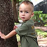 child, toddler, boy, portrait, outdoors, tree, nature, garden, greenery, forest, standing, looking_at_camera, curious, short_hair, t_shirt, camouflage_shorts, sunlight, bokeh, tree_trunk, path