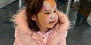 Niomie is registered to the contest to win money with this photo: child, face_paint, pink_coat, smiling, indoor, girl, scrunchie, reflection, glass_door, happy, winter_clothing, cute, portrait, ruffles, young_child, people, floor_tiles, casual_wear, person, coat