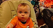 Phoenix is registered to the contest to win money with this photo: baby, child, high_chair, orange_shirt, person, elderly_person, water_bottle, glasses, indoor, living_room, curtains, lamp, walker, furniture, table, vase, flowers, seated, expression, reaching_hand