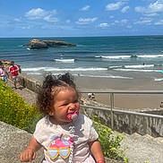 Khäyla participe au concours pour gagner de l'argent avec cette photo : toddler, child, pacifier, curly_hair, beach, ocean, sky, clouds, sunny, stone_wall, tshirt, skirt, flowers, people, summer, outdoor, happy, smiling, nature, water