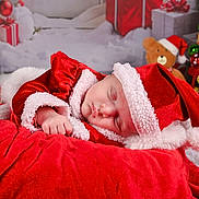 Keyla a rejoint le concours — aidez-le/la à gagner de superbes lots ! baby, sleeping, santa_hat, christmas, holiday, red_clothing, blanket, teddy_bear, gift_box, christmas_tree, decorations, festive, soft_texture, cute, portrait, indoor, holiday_season, infant, cozy, sleep