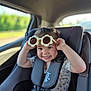 car_interior, car_seat, casual_clothing, child, curly_hair, cute, daylight, flower_shaped_glasses, happy, patterned_shirt, pink_pants, playful, portrait, safety_harness, seat, seatbelt, smiling, sunglasses, toddler, window