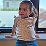 casual_clothing, child, curious, daylight, face, floral_print, girl, hair_tied_back, hands, indoor, jeans, natural_light, playful, portrait, sitting, toddler, top, window, windowsill, young_child
