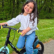 Elianah participe au concours pour gagner de l'argent avec cette photo : bicycle, bike_ride, casual_clothing, child, curly_hair, footwear, greenery, happy, jeans, nature, outdoor, park, pavement, play, smiling, sunny_day, training_wheels, trees, white_shirt, young_child