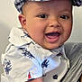baby, child, smiling, cap, hat, shirt, patterned_clothing, indoor, person, face, happy, cute, portrait, infant, closeup, cheerful, apparel, holding, arm, skin