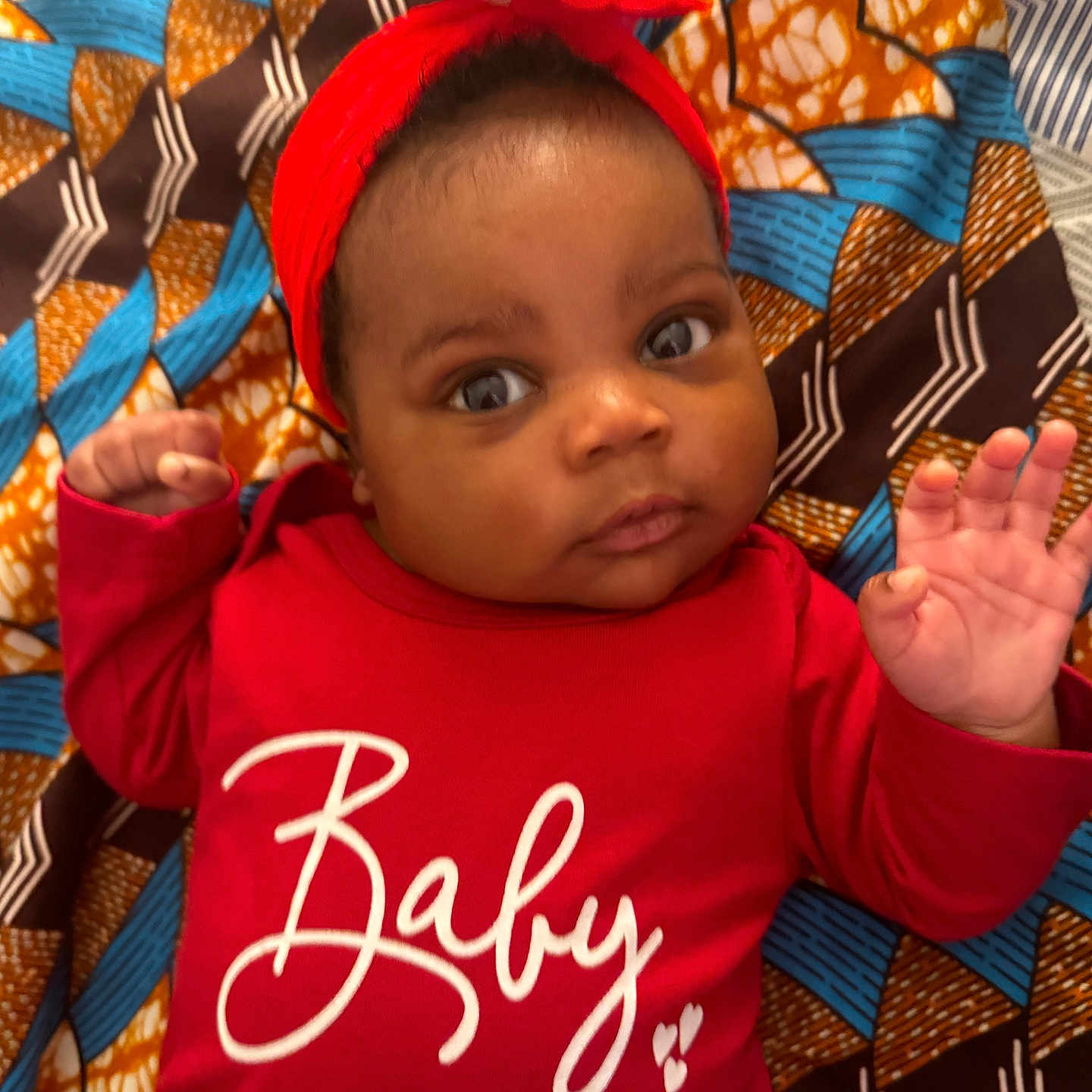 Eliana is registered to the contest to win money with this photo: accessories, applique, baby, bodypart, clothing, couch, face, finger, furniture, hand, happy, head, headband, pattern, person, photography, portrait, quilt, shorts, t_shirt