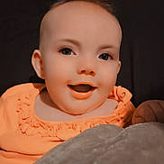 Delilah is registered to the contest to win money with this photo: baby, child, smiling, orange_clothing, blanket, face, portrait, indoor, cozy, happy, infant, cute, head, person, expression, sitting, warm, young_child, closeup, background