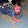baby, child, person, floor_mat, striped_clothing, indoor, adult, hand, sitting, tummy_time, playtime, puzzle_mat, blue, white, socks, hair, curly_hair, casual, home, carpet