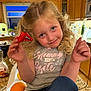 child, girl, blonde_hair, curly_hair, smile, kitchen, counter, candy, red_wrapper, green_candy, casual_clothing, grey_shirt, text_on_shirt, orange, pancake_syrup, indoor, portrait, happy, holding, playful
