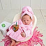 baby, sleeping, pink_robe, turban, iced_coffee, cup, chair, cucumber_slices, table, pink_rug, curly_rug, infant, cozy, relaxed, indoor, wooden_floor, cute, small_hands, foot, portrait