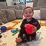 Gael joined the competition — help win amazing prizes! baby, child, indoor, playmat, toy, ball, pajamas, smile, couch, pillow, living_room, giraffe_pattern, red_ball, blue_ball, stuffed_toy, happy, playtime, floor_mat, footwearless, young_child