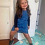 Kenza a rejoint le concours — aidez-le/la à gagner de superbes lots ! child, girl, smiling, denim_dress, black_sneakers, curly_hair, indoor, floor_mat, unicorn, playful_pose, joyful, happy, person, clothing, footwear, room, door, cabinet, flooring, casual