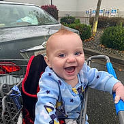Zander is registered to the contest to win money with this photo: baby, child, shopping_cart, blue_onesie, smiling, happy, outdoor, parking_lot, car, rain, wet_surface, mohaawk_hairstyle, clothing, person, infant, cute, joyful, expression, holding, seat