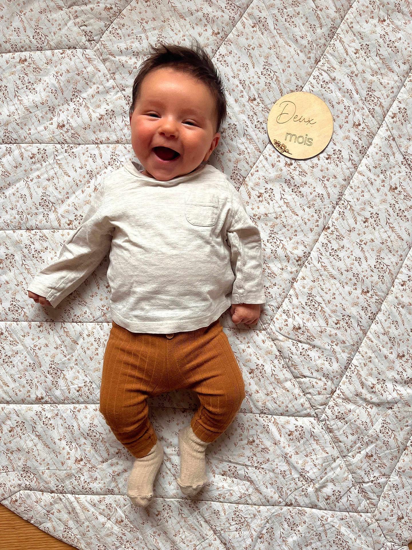 Gaspard participe au concours pour gagner de l'argent avec cette photo : baby, child, cute, expression, face, hair, happy, indoors, infant, lying_down, patterned, portrait, quilt, rust_pants, smiling, socks, soft_light, two_months, white_shirt, wooden_sign