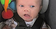 Noah is registered to the contest to win money with this photo: baby, infant, child, car_seat, harness, buckled, portrait, face, eyes, open_mouth, sitting, indoor, toy, colorful, plush_toy, automotive, safety, clothing, hands, close_up