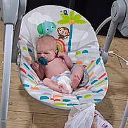 Noah joined the competition — help win amazing prizes! baby, infant, child, bouncer, pacifier, sitting, lying_down, face, feet, toys, elephant, monkey, colorful, indoor, wooden_floor, baby_gear, chair, blanket, home, portrait
