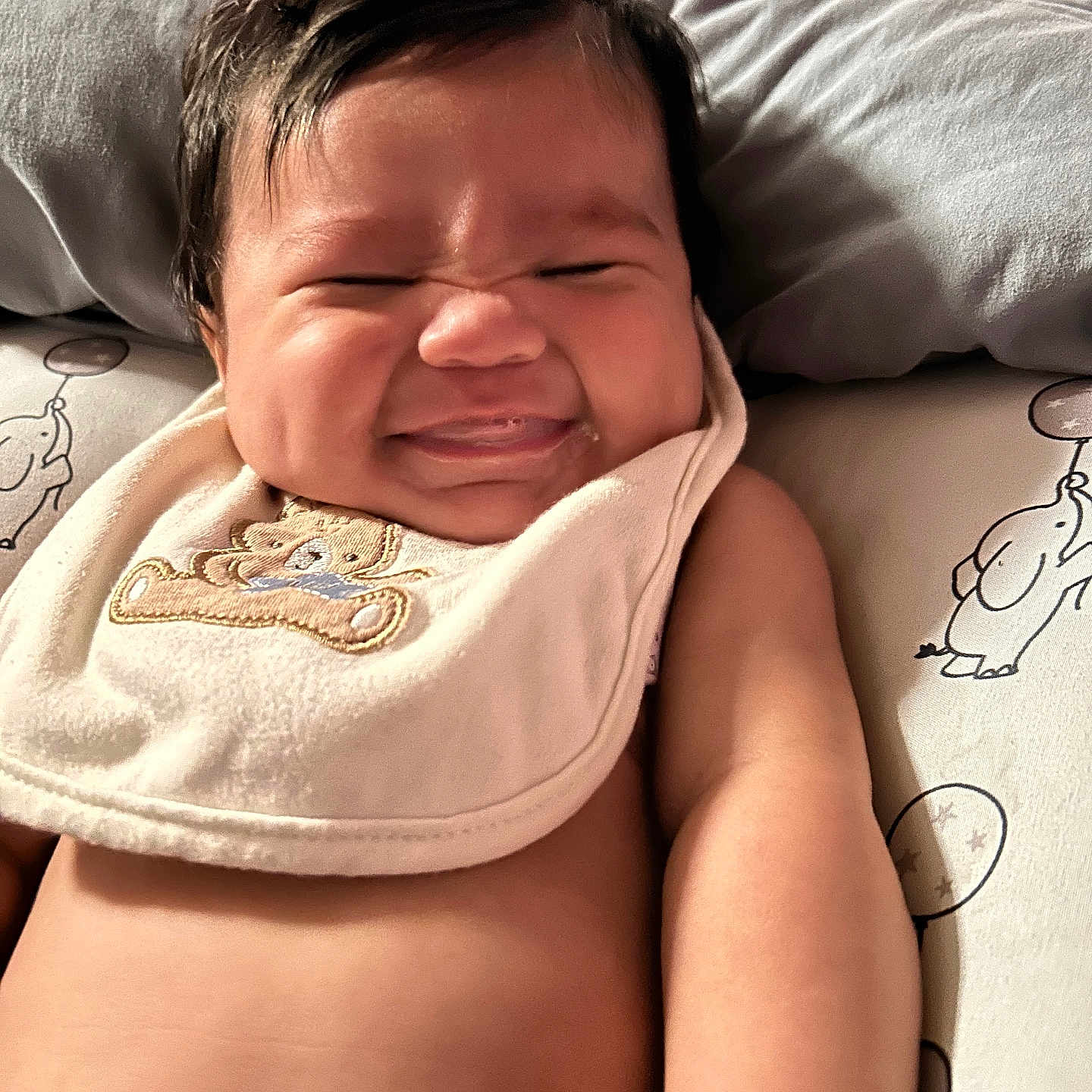 Ezereth is registered to the contest to win money with this photo: adorable, arm, baby, bib, child, chubby, closeup, cute, elephant, expression, face, happy, indoors, infant, lying_down, person, pillow, skin, smile, teddy_bear