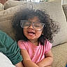 Hailee joined the competition — help win amazing prizes! child, toddler, glasses, curly_hair, smiling, pink_shirt, couch, living_room, happy, face, person, seated, indoors, casual, cute, young_child, relaxed, home, portrait, fun