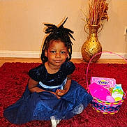 Sarai is registered to the contest to win money with this photo: child, girl, blue_dress, braided_hair, carpet, red_rug, easter_basket, toys, marshmallows, indoor, floor, vase, decor, wood_floor, smiling, sitting, home, cute, portrait, holiday