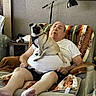 Chichi joined the competition — help win amazing prizes! elderly_man, pug, dog, sleeping, armchair, blanket, reading_lamp, bookshelf, casual_clothing, white_tshirt, shorts, living_room, relaxing, indoor, pet, resting, comfort, home, furniture, napping