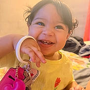 Amira Sophia joined the competition — help win amazing prizes! toddler, child, smiling, keys, keychain, yellow_shirt, flower, happy, indoors, bed, curly_hair, cute, closeup, person, hand, playful, bright, young_child, portrait, warm_light